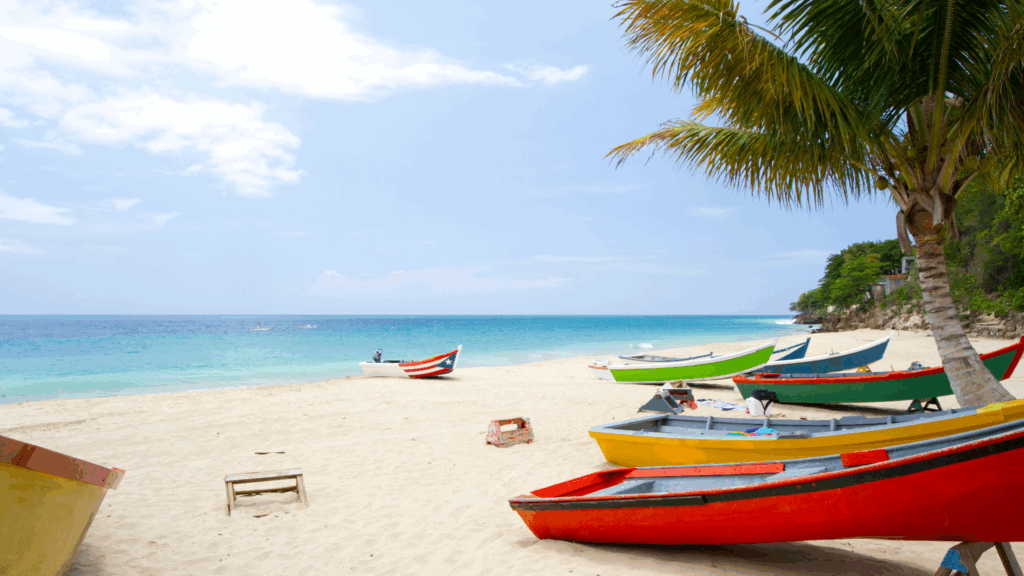 A beautiful, almost cloud-free day on a peaceful beach in Puerto Rico with multiple small boats in the sand, with one of them having the flag painted. 